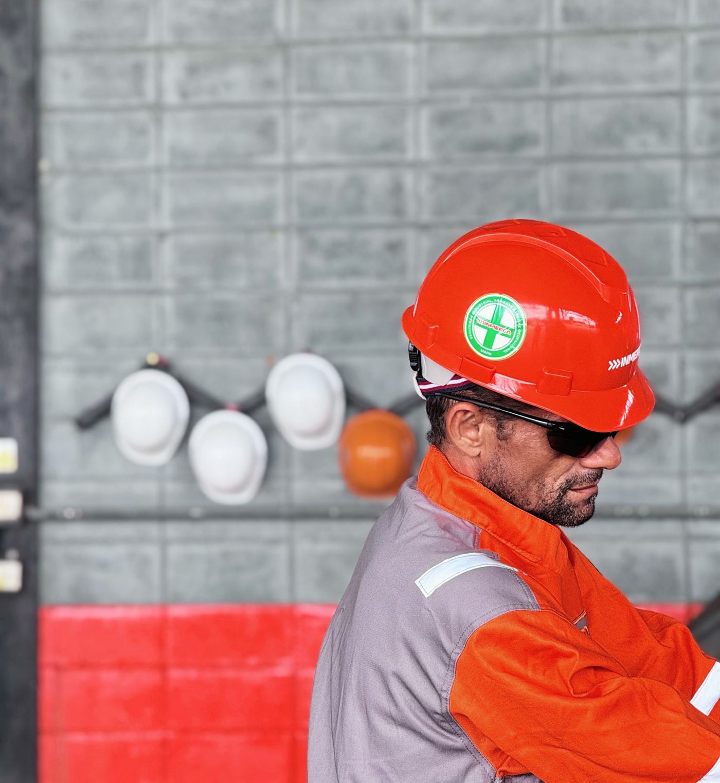 Trabajador de INMERCA con casco naranja y braga reflectiva frente a la pared de cascos del taller
